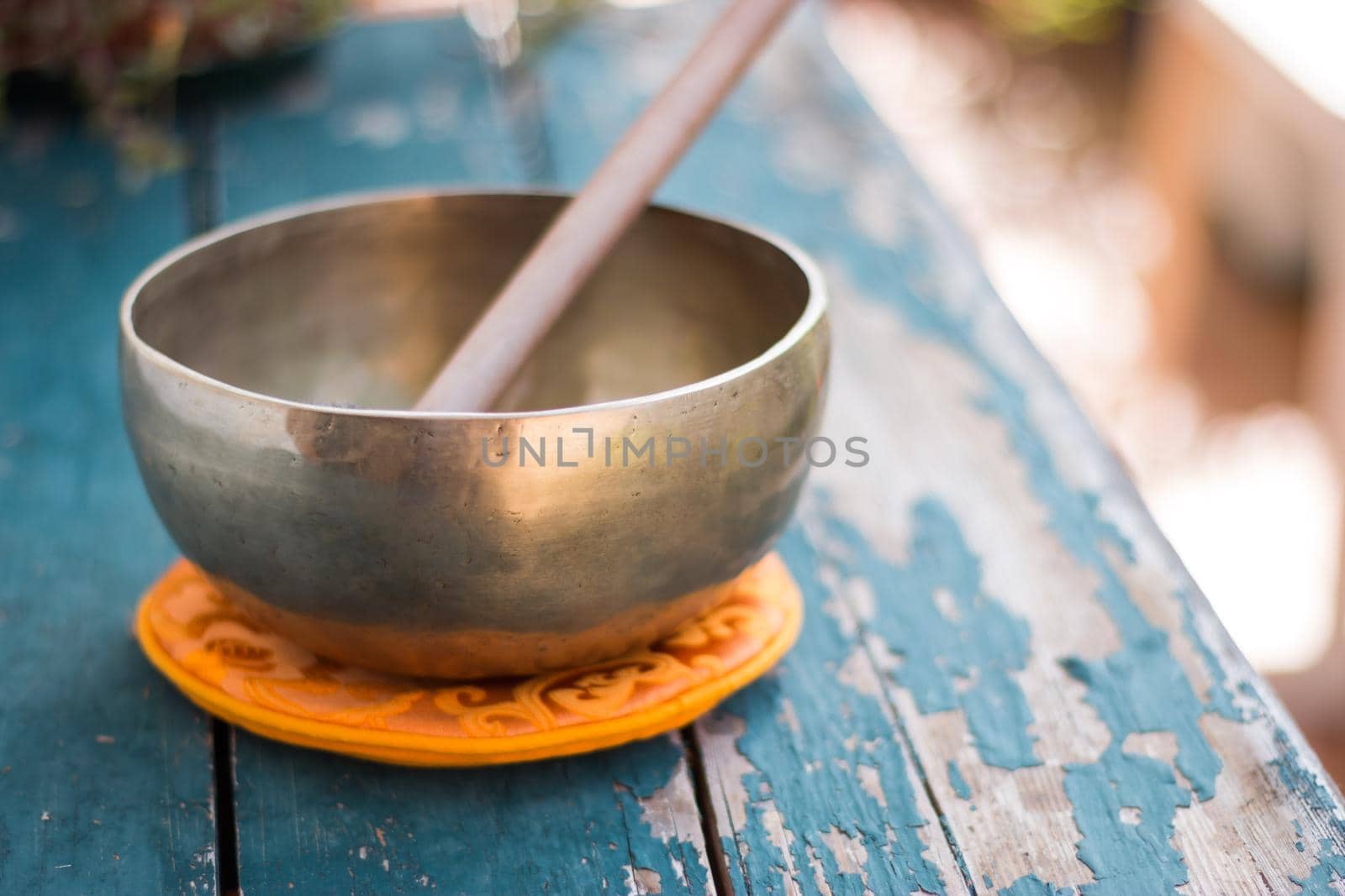 Metal singing bowl on a rustic green, wooden table outdoors. Flowers in the colourful, blurry background