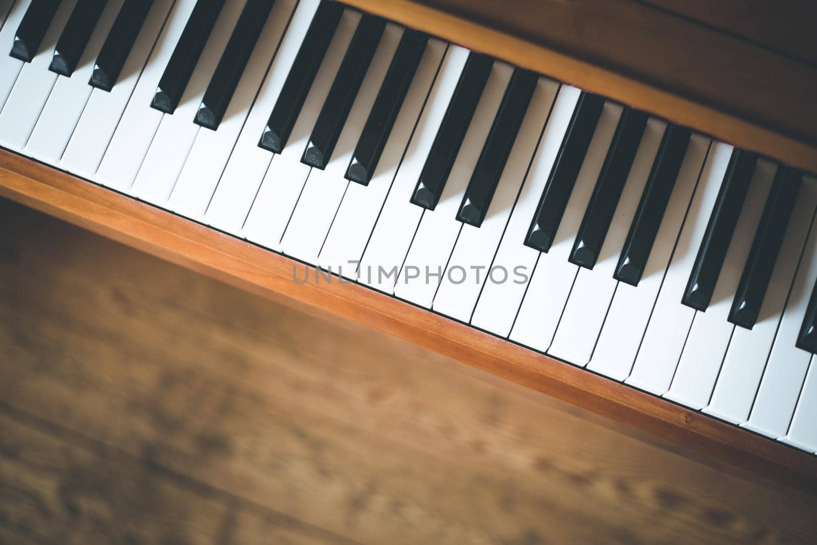 Vintage wooden piano. Keys in the foreground, wooden floor with text space in the blurry background by Daxenbichler
