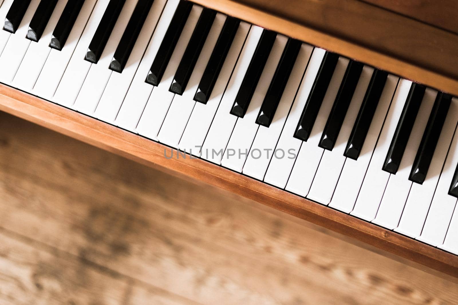 Vintage wooden piano. Keys in the foreground, wooden floor with text space in the blurry background by Daxenbichler