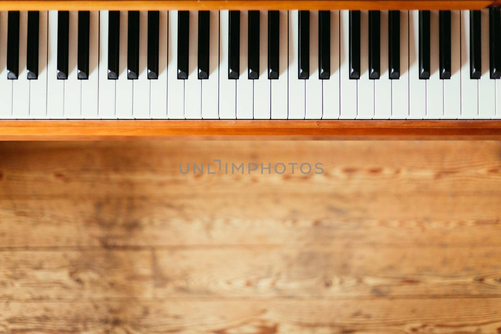 Vintage wooden piano. Keys in the foreground, wooden floor with text space in the blurry background by Daxenbichler