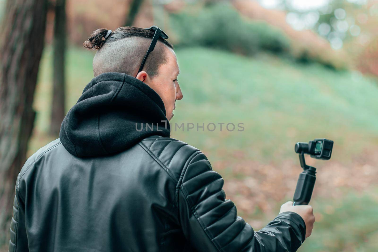 Blogger in Black Clothes and Sunglasses Making Video Using Action Camera with Gimbal Camera Stabilizer in Autumn Park