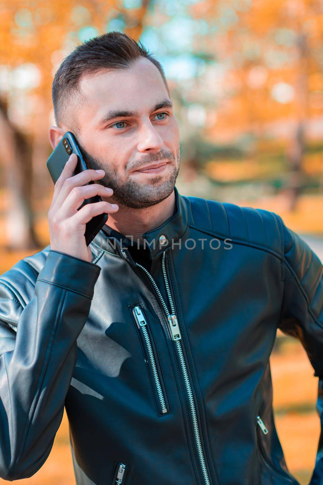 Handsome Young Man Talking on the Phone at the Beautiful Autumn Park. Youthful Guy Using Smartphone for the Call Outdoors at Sunny Day