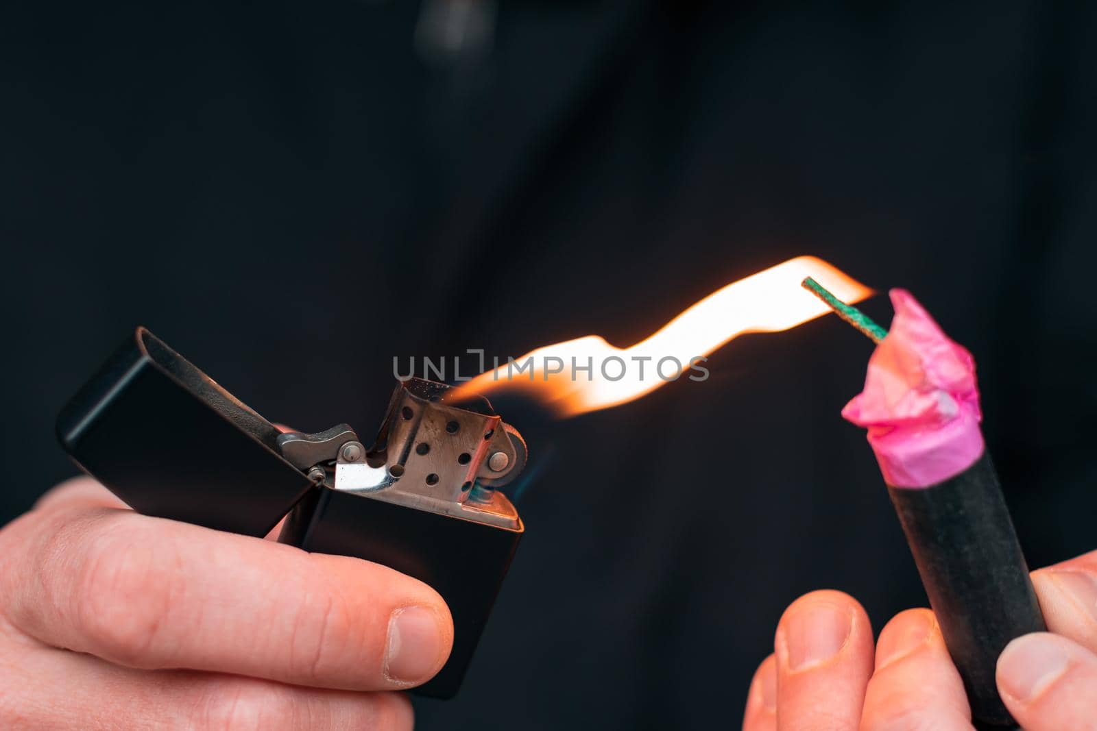 Setting Fire to the Firecracker. Man in Black Clothes Lighting Up the Petard. Firing Up the Pyrotechnics with a Black Gasoline Lighter Outdoors