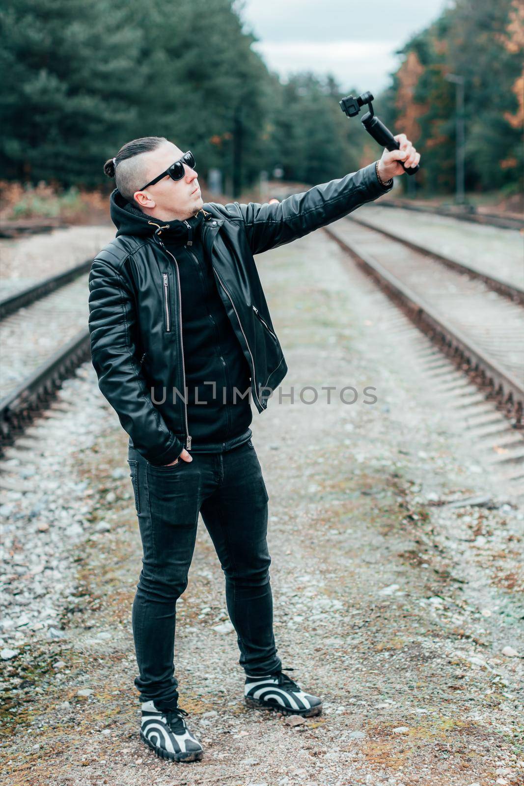 Blogger in Sunglasses Making Selfie or Streaming Video at the Pine Forest Using Action Camera with Gimbal Camera Stabilizer. Handsome Man in Black Clothes Making Photo