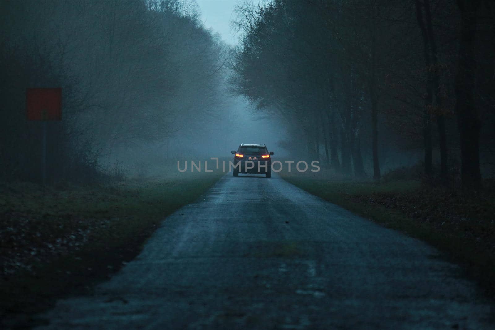 Asphalt road after the rain in the evening on a foggy day with a car in the background