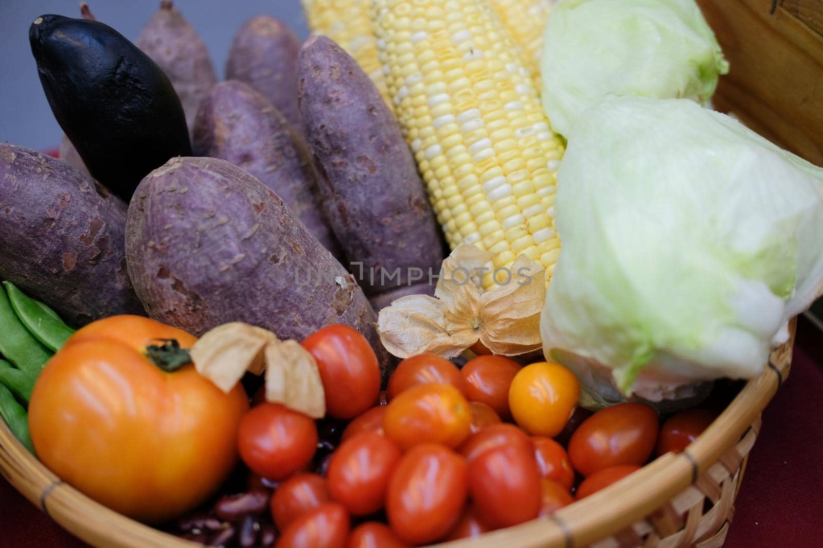 gooseberries, corn, purple sweet potato, tomatoes and lettuce in wicker basket. vegetable harvest from farm