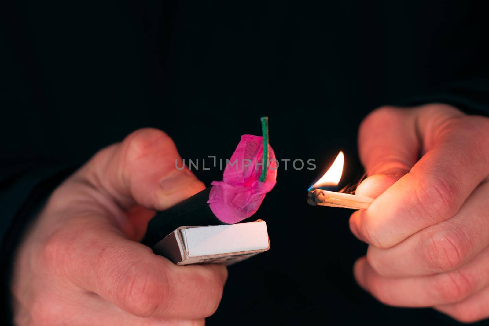 Setting Fire to the Firecracker. Man in Black Clothes Lighting Up the Petard. Pyrotechnics Firing Up with Matches Holding Together with a Matchbox Outdoors