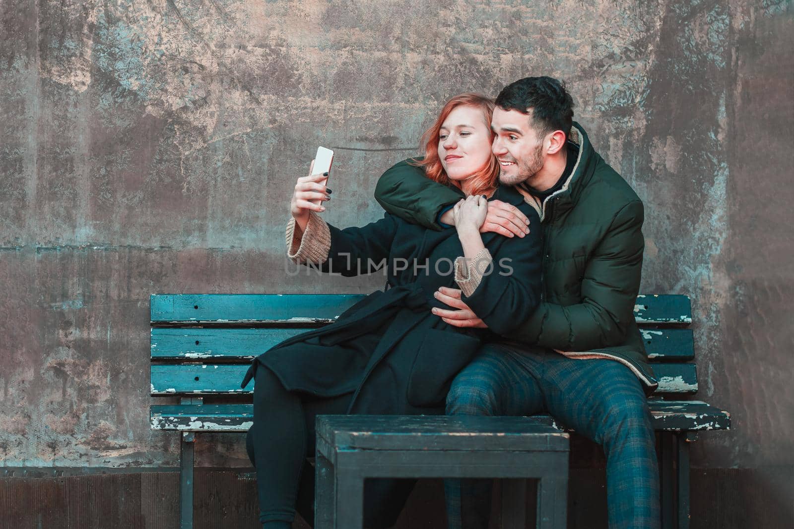 Cheerful Emotional Young Couple Sitting on the Bench and Making Selfie. Two Happy People Love Story on the Street