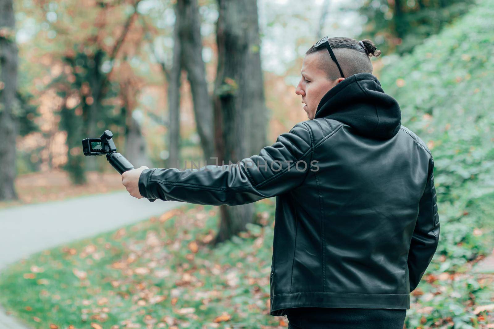 Blogger in Black Clothes and Sunglasses Making Video Using Action Camera with Gimbal Camera Stabilizer in Autumn Park