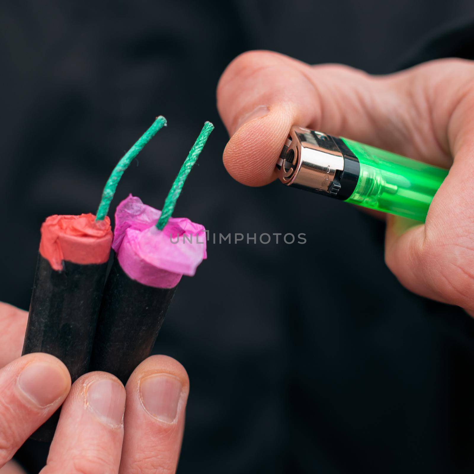 Setting Fire to the several Firecrackers. Man in Black Clothes Lighting Up Two Petards at the Same Time. Firing Up the Pyrotechnic with Green Gas Lighter Outdoors