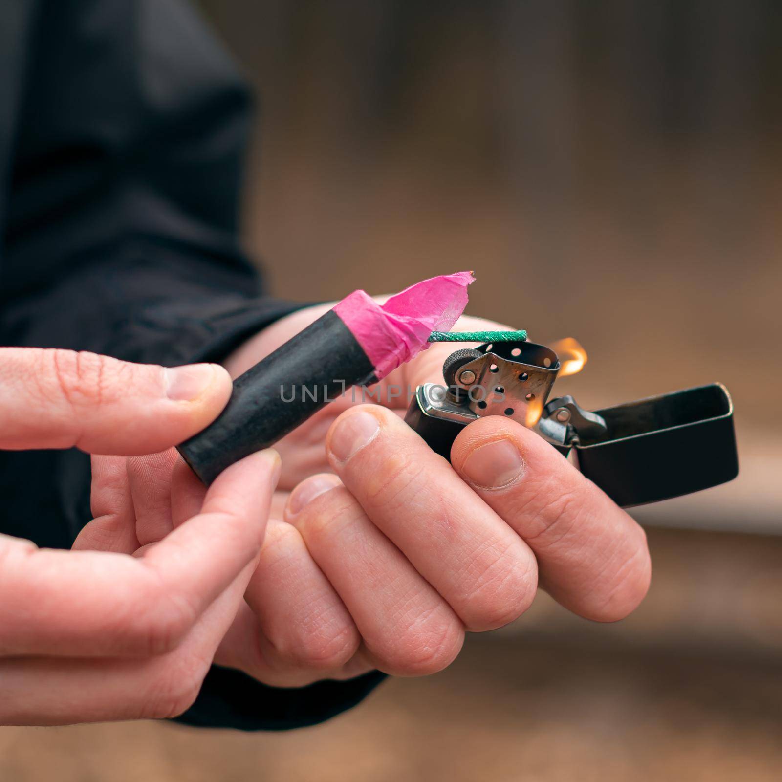 Setting Fire to the Firecracker. Man in Black Clothes Lighting Up the Petard. Firing Up the Pyrotechnics with a Black Gasoline Lighter Outdoors