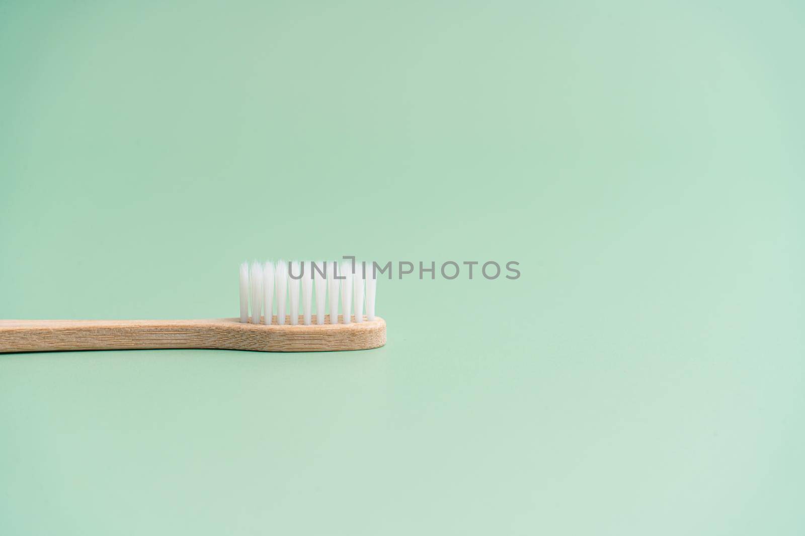 Environmentally friendly bamboo wood antibacterial toothbrush on light green background.