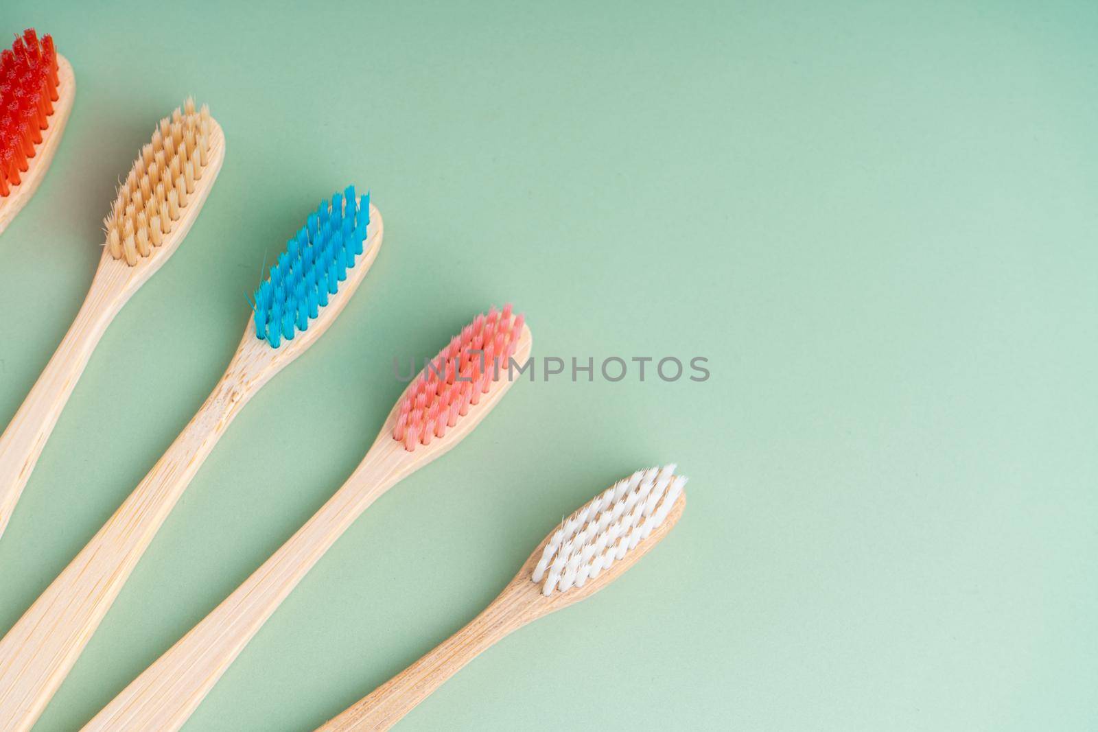 A set of Eco-friendly antibacterial toothbrushes made of bamboo wood on a light green background. Environmental care trends.