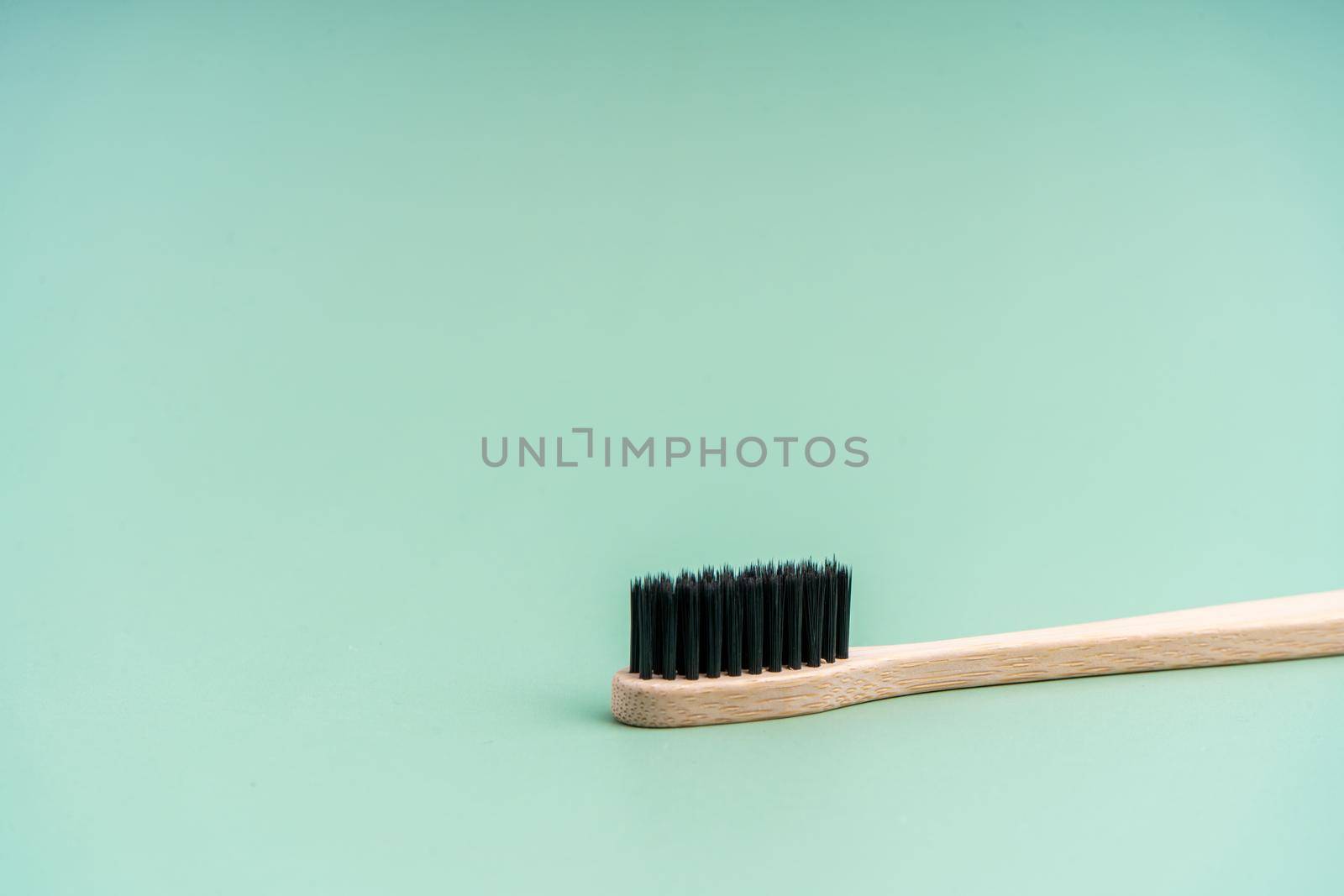 Eco friendly antibacterial bamboo wood toothbrush with black bristles on light green background. Taking care of the environment in trend.