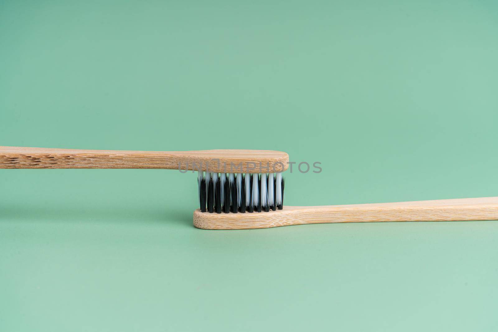 Two Eco-friendly antibacterial bamboo wood toothbrushes with white and black bristles on a light green background. Taking care of the environment is trending. Tolerance. Copy space by Try_my_best