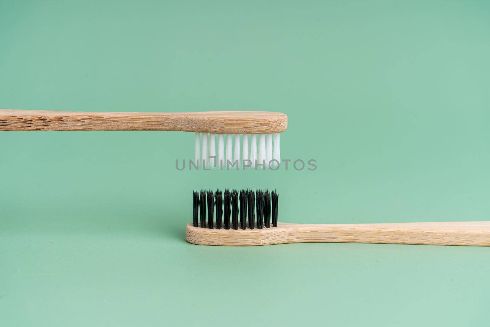 Two Eco-friendly antibacterial bamboo wood toothbrushes with white and black bristles on a light green background. Taking care of the environment is trending. Tolerance. Copy space by Try_my_best