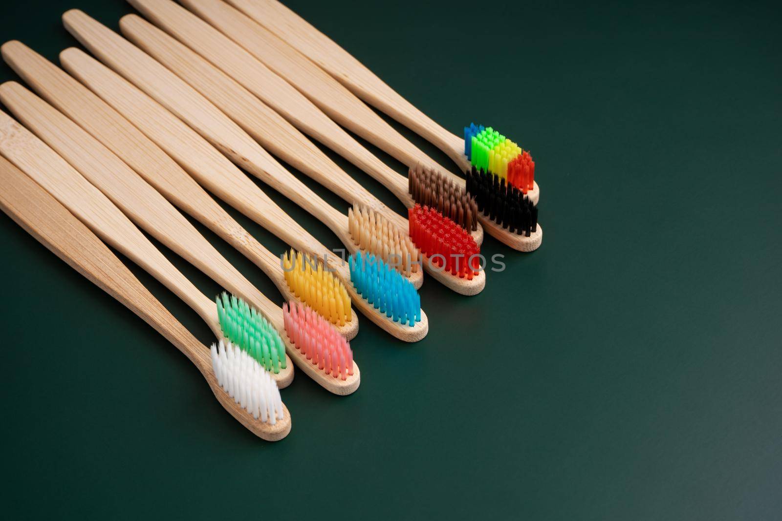 A set of Eco-friendly antibacterial toothbrushes made of bamboo wood on a dark green background. Environmental trends.