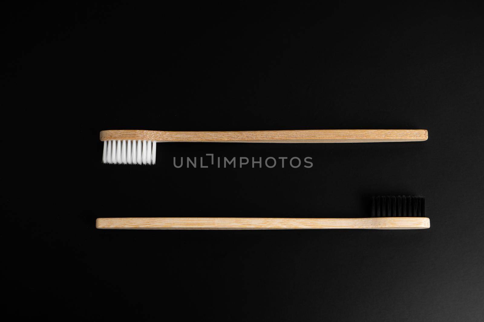 Two Eco-friendly antibacterial bamboo wood toothbrushes with white and black bristles on a black background. Taking care of the environment is trending. Tolerance. Copy space.