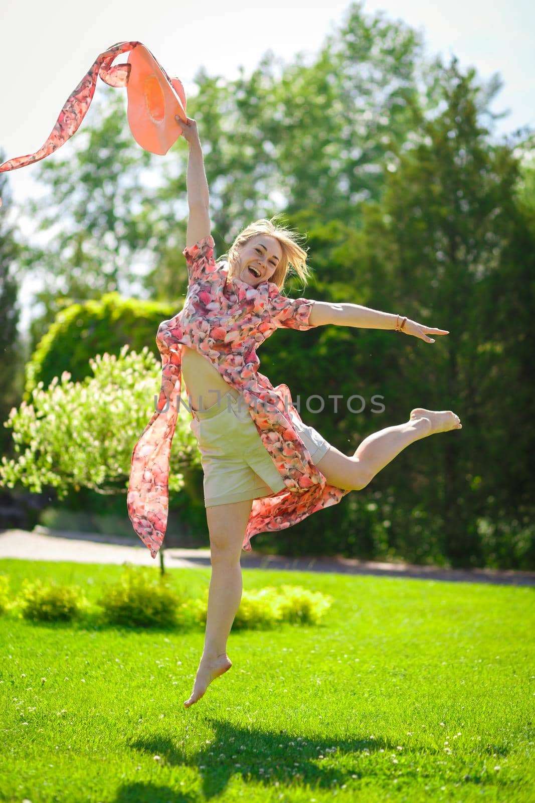 A charming girl in a light summer sundress and a pareo hat is walking in a green park. Enjoys warm sunny summer days.