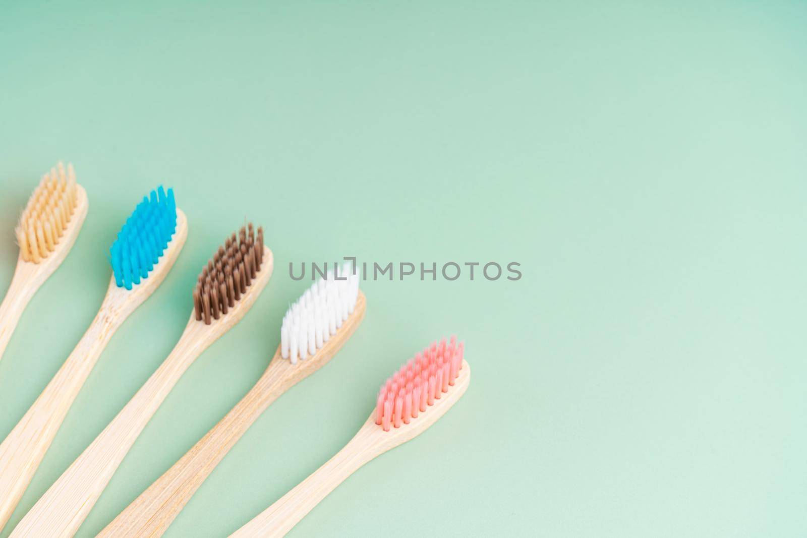 A set of Eco-friendly antibacterial toothbrushes made of bamboo wood on a light green background. Environmental care trends by Try_my_best