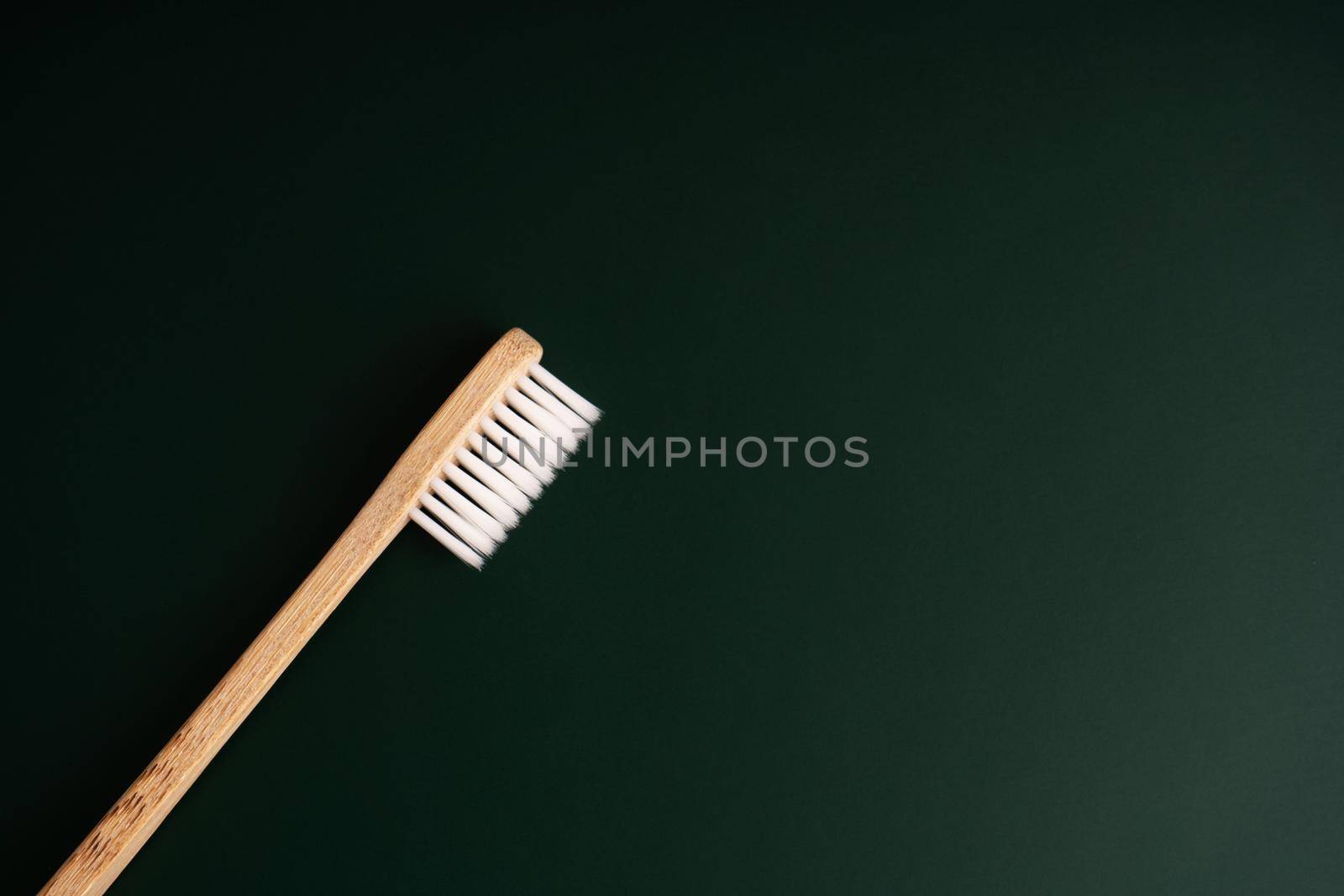 Eco friendly dental health antibacterial bamboo wood toothbrush on dark green background.