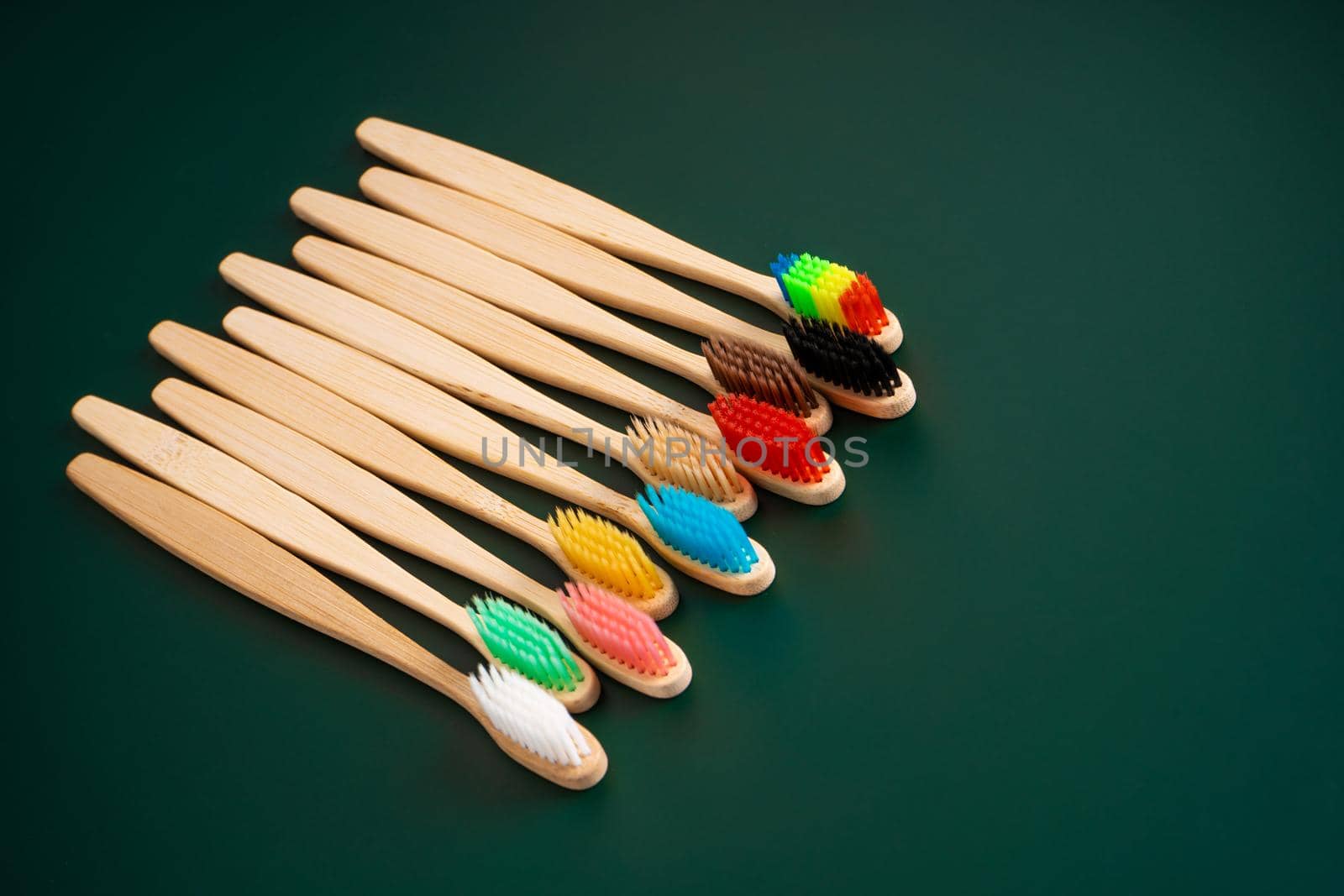 A set of Eco-friendly antibacterial toothbrushes made of bamboo wood on a dark green background. Environmental trends.