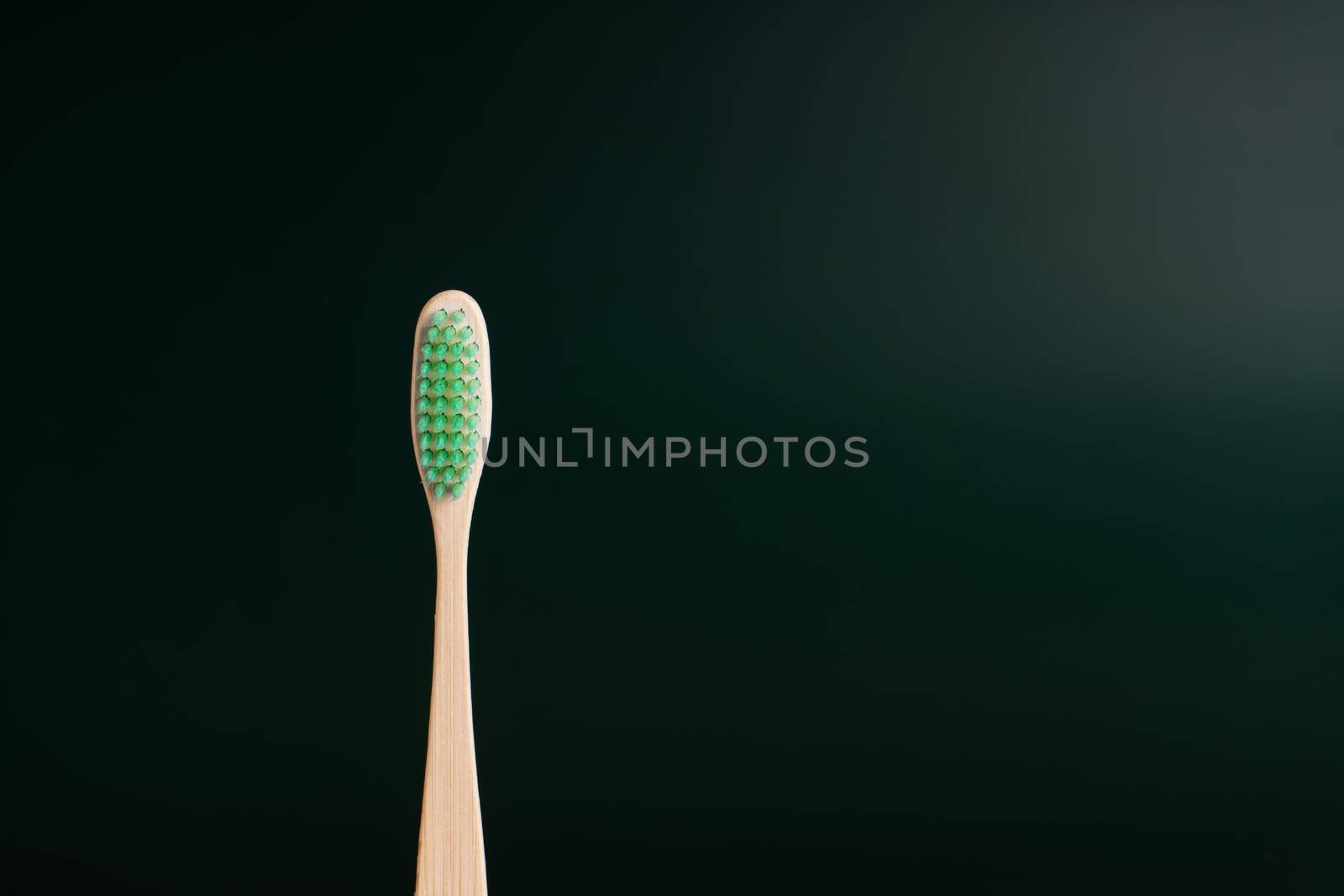 Eco-friendly antibacterial bamboo wood toothbrush on dark green background. Taking care of the environment in trend.