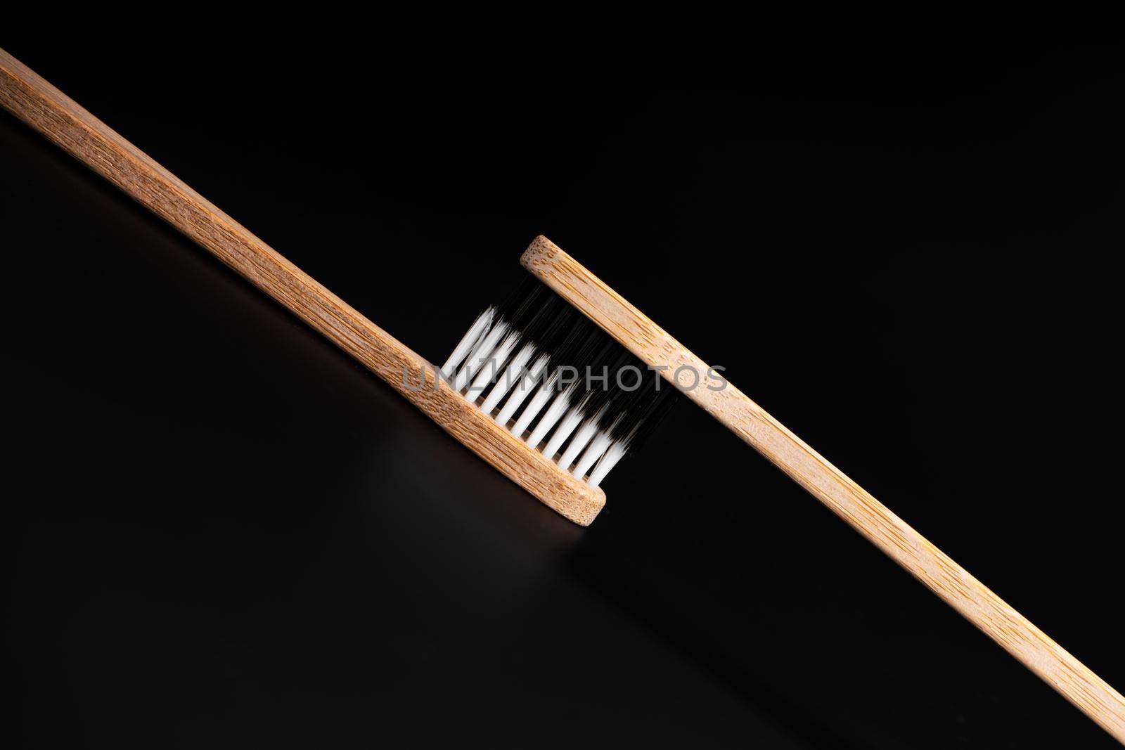 Two Eco-friendly antibacterial bamboo wood toothbrushes with white and black bristles on a black background. Taking care of the environment is trending. Tolerance. Copy space.