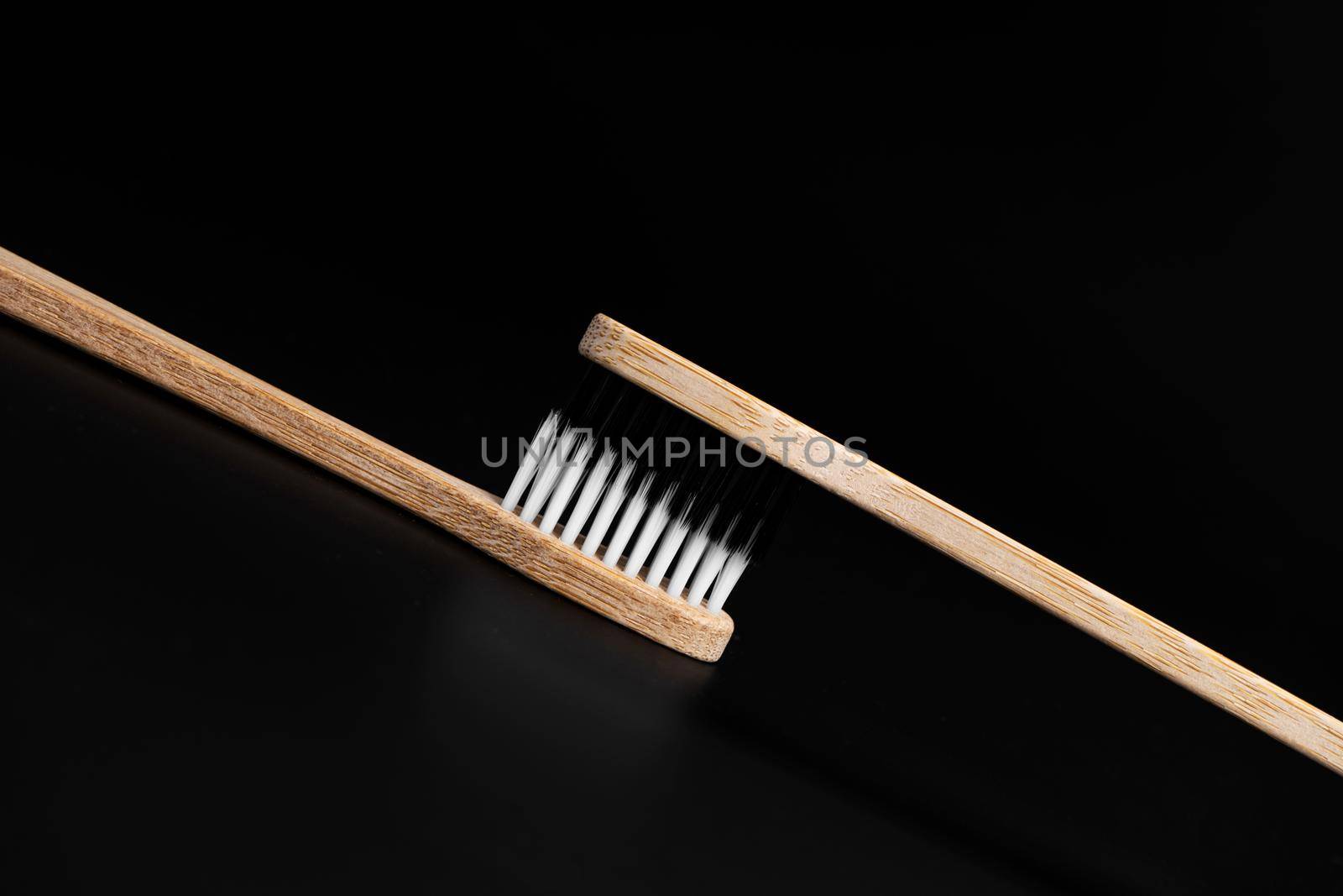 Two Eco-friendly antibacterial bamboo wood toothbrushes with white and black bristles on a black background. Taking care of the environment is trending. Tolerance. Copy space by Try_my_best
