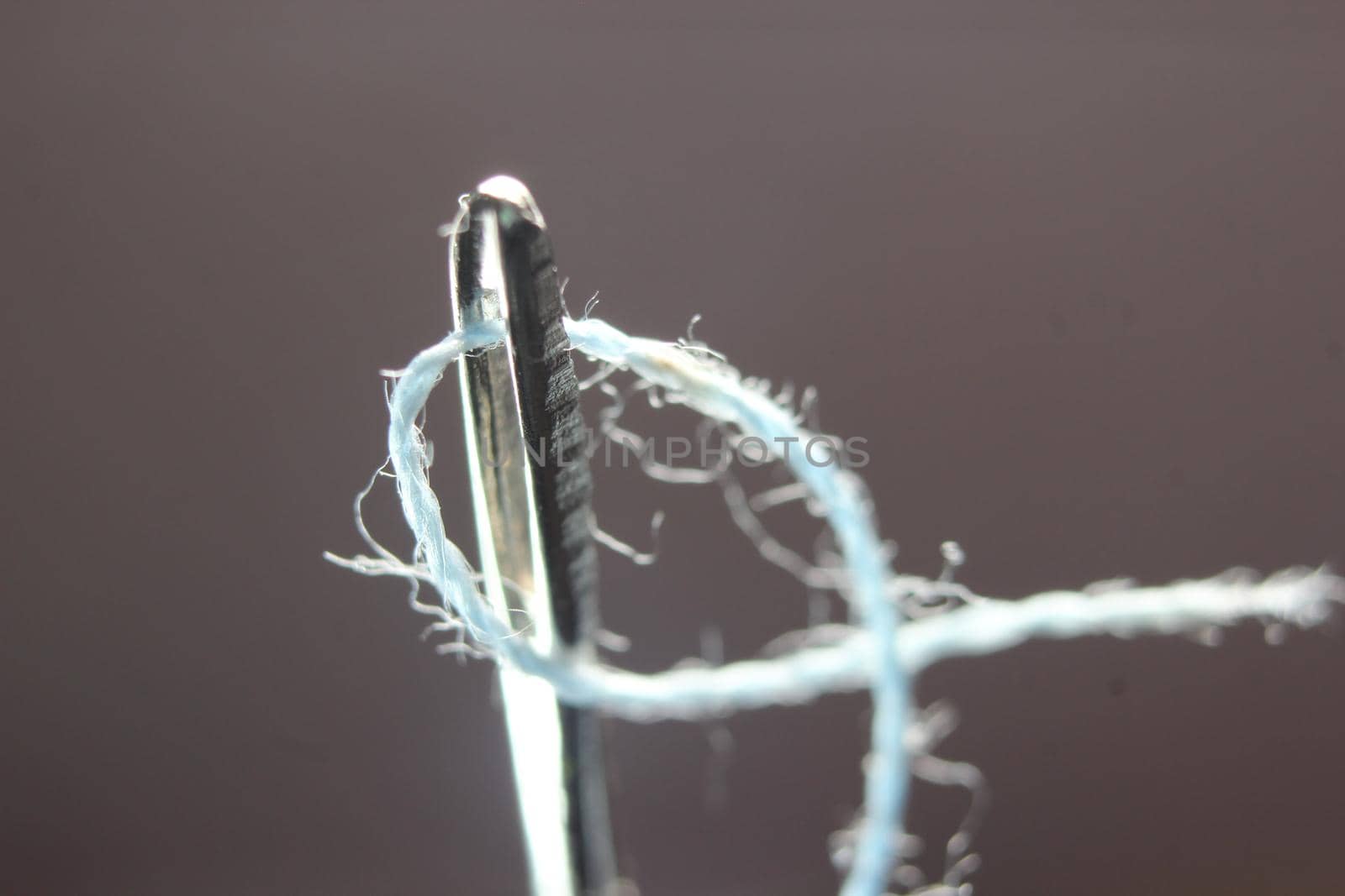 Macro photograph of sewing needle. Small needle with thread in the eyelet, isolated over the black background.