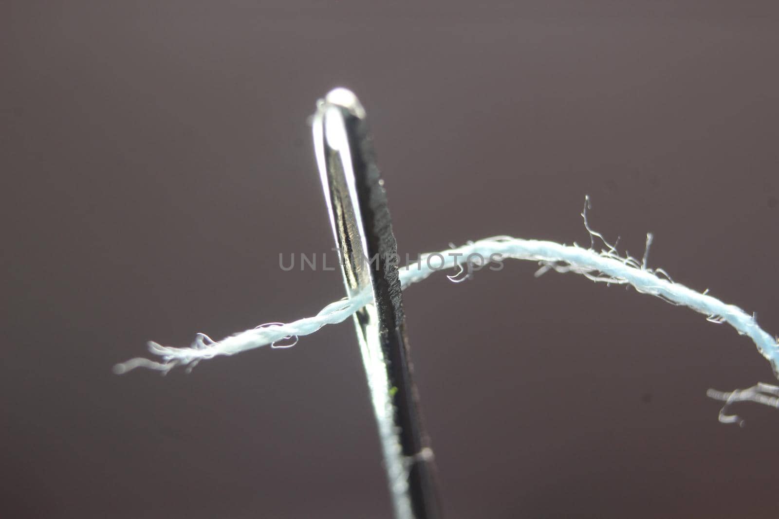 Macro photograph of sewing needle. Small needle with thread in the eyelet, isolated over the black background.