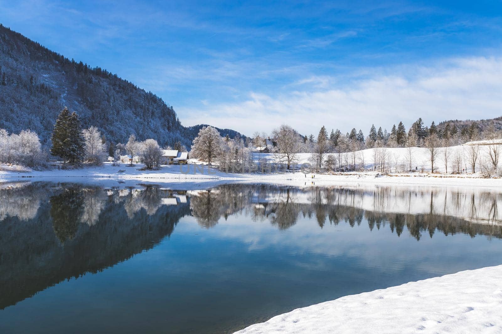 Idyllic winter landscape: Reflection lake, house and snowy trees and mountains