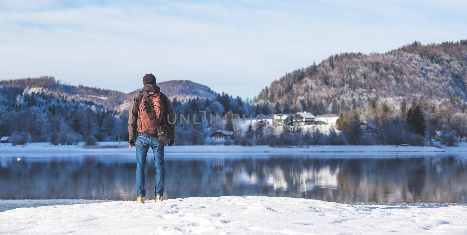 Sporty Caucasian man is at the lakeshore, enjoying the view. Winter landscape.