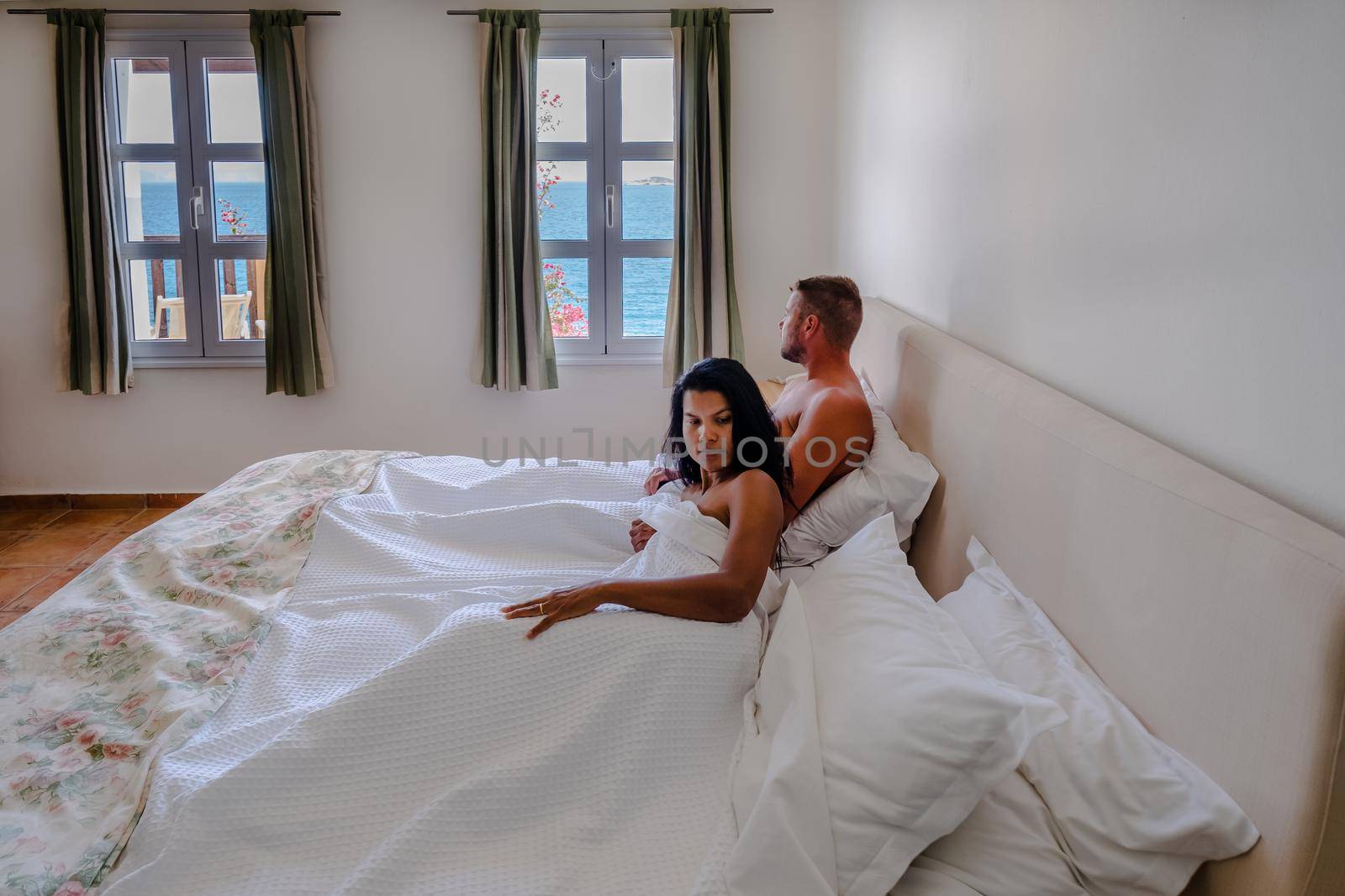 couple in white bed looking out over ocean during luxury vacation in Greece. High quality photo