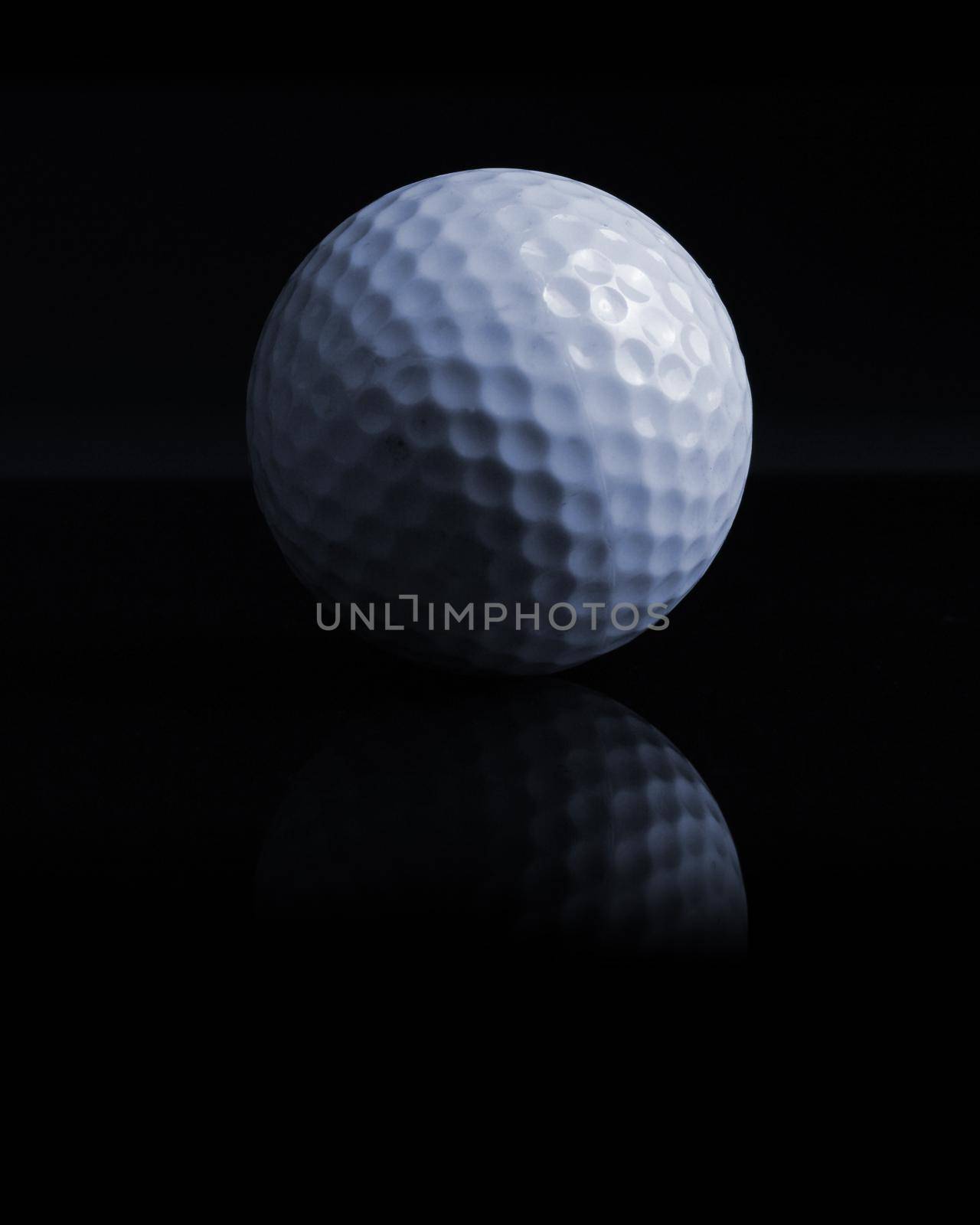 An isolated over black reflective surface of a common golf ball showing the details using shadow and light contrast.