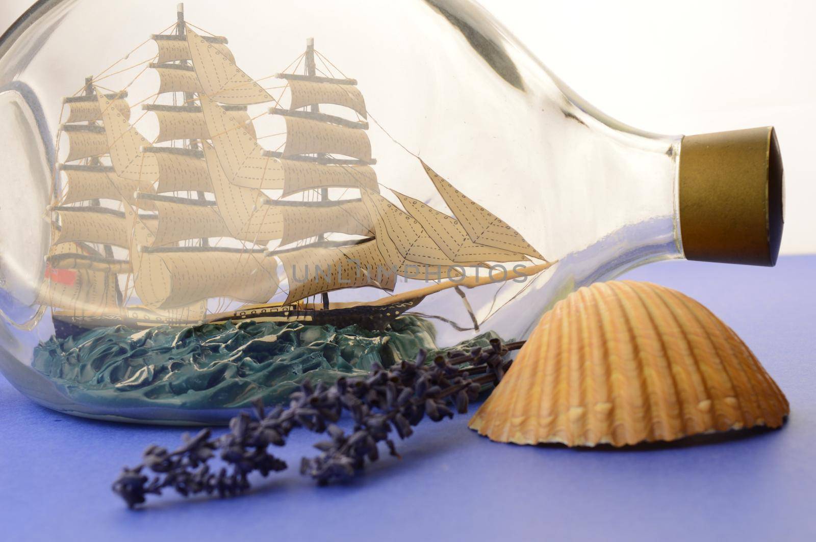 A calming scene of blues and a anutical ship in a bottle with a seashell and lavender.