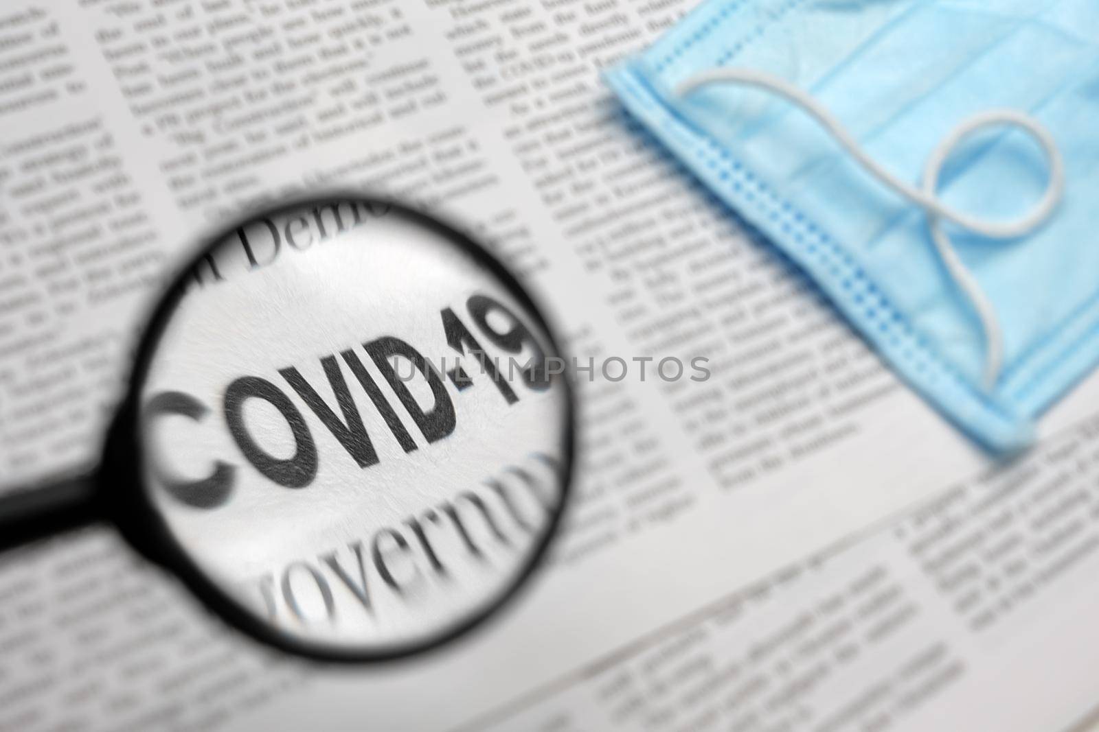 Newspaper Article with the Headline Covid 19. News about Coronavirus Pandemic on a newspaper through a magnifying glass. News Related to the corona virus. Medical mask. Face Mask. News media Concept