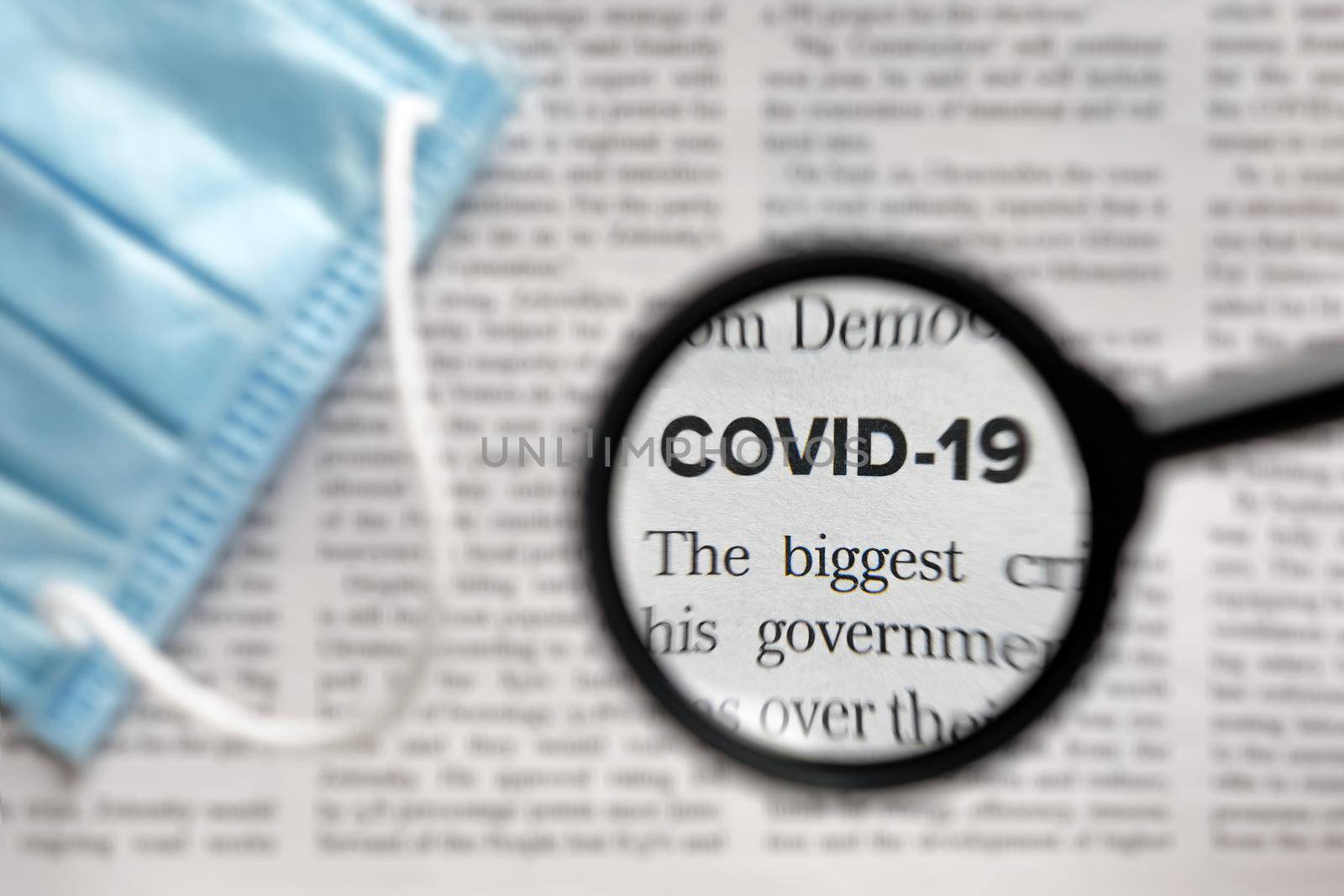 Newspaper Article with the Headline Covid 19. News about Coronavirus Pandemic on a newspaper through a magnifying glass. News Related to the corona virus. Medical mask. Face Mask. News media Concept by synel