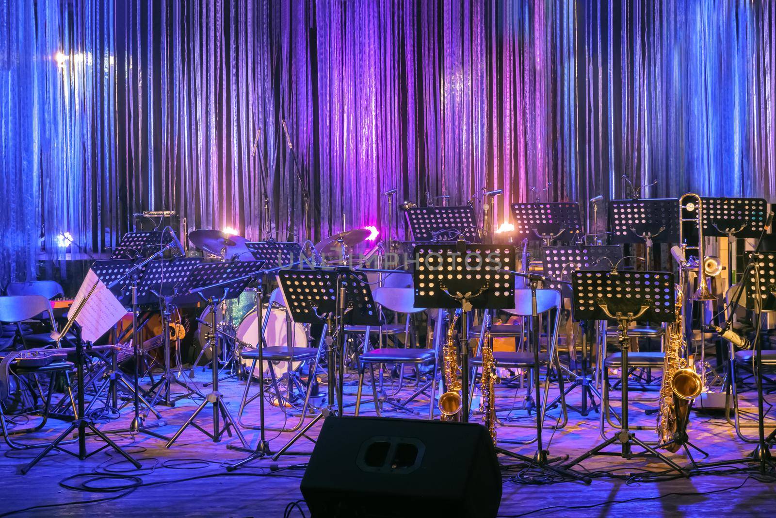 Musical Instruments and Sheet Music Standing Ready on a Stage for a Live Performace at Rock or Jazz Concert or Festival in Colourful Lighting. Empty Stage for Orchestra. Online Music Concert or Event by synel