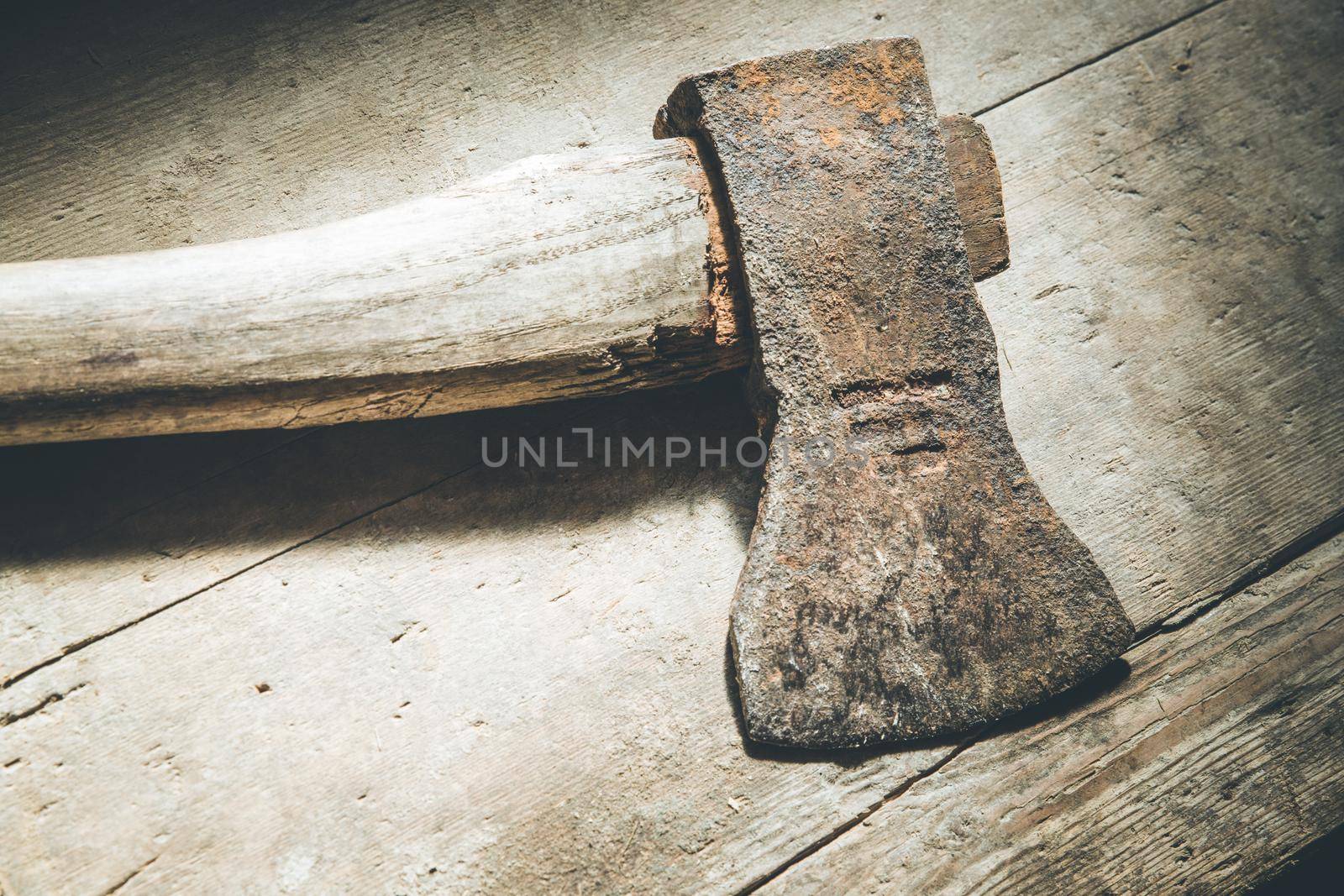 Old rusty axe is lying on rustic wooden floor by Daxenbichler