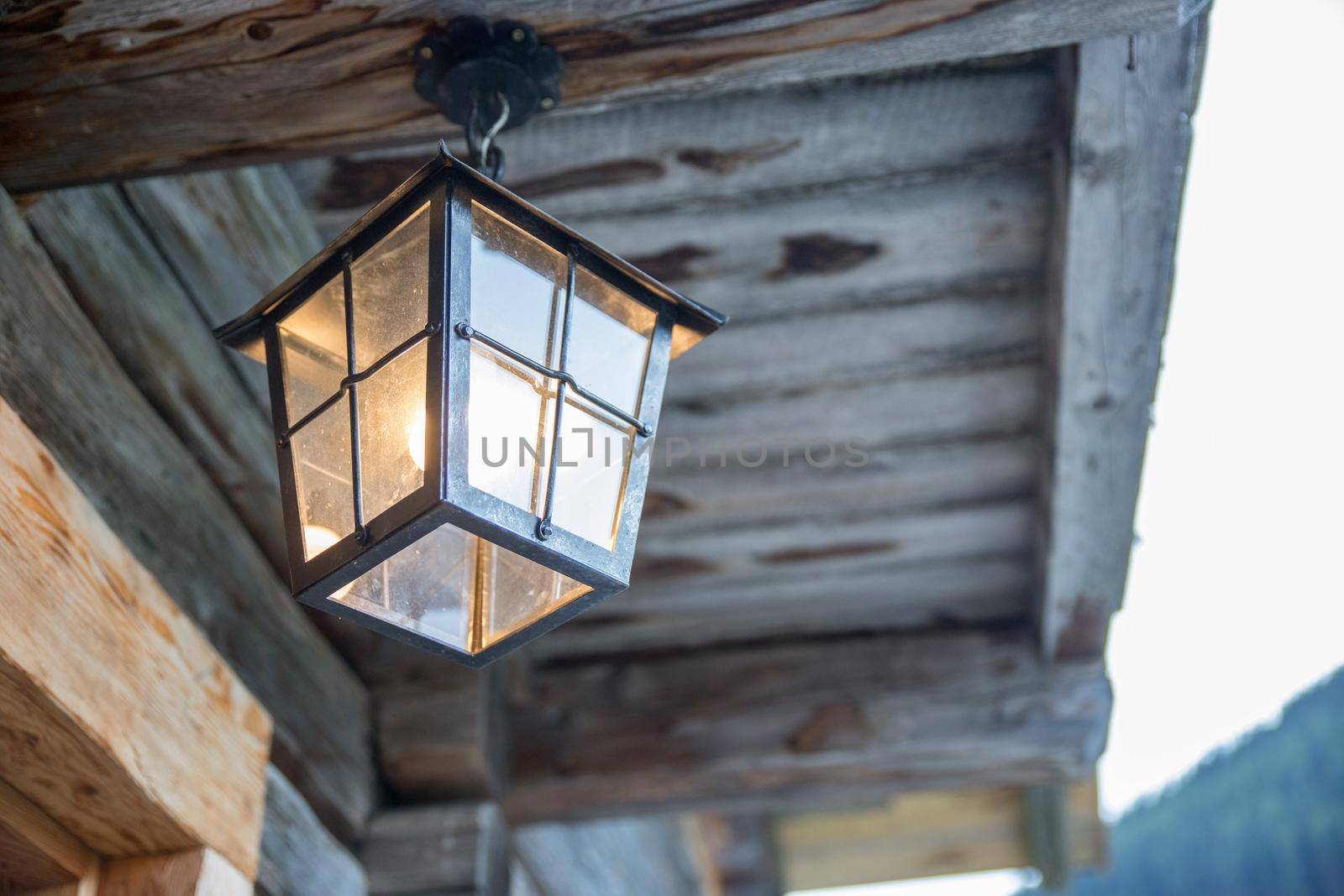 Rustic lantern is shining over the veranda, alpine hut