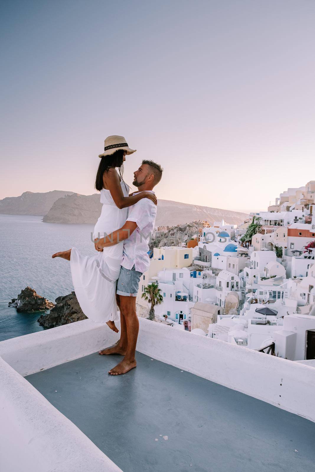 Santorini Greece, young couple on luxury vacation at the Island of Santorini watching sunrise by the blue dome church and whitewashed village of Oia Santorini Greece . Europe