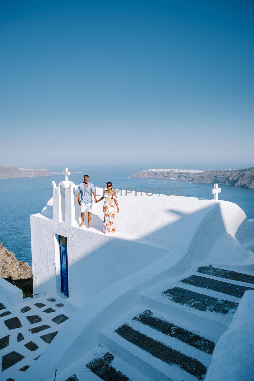 couple visit Skaros rock Fira, Santorini Greece, young couple on luxury vacation at the Island of Santorini watching sunrise by the blue dome church and whitewashed village of Oia Santorini Greece  by fokkebok