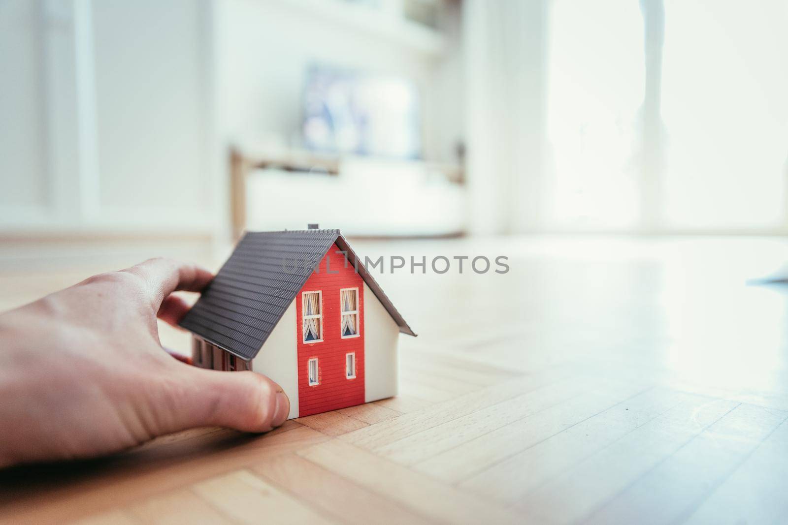 Adult hand is holding red house model, indoors. Concept for new home, property and estate