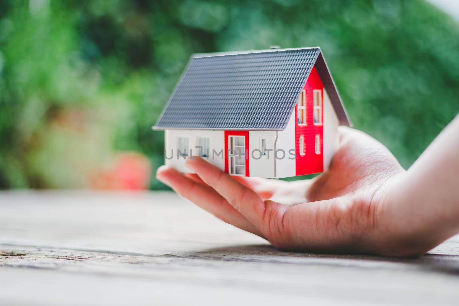 Adult hand is holding red house model, outdoors. Concept for new home, property and estate by Daxenbichler