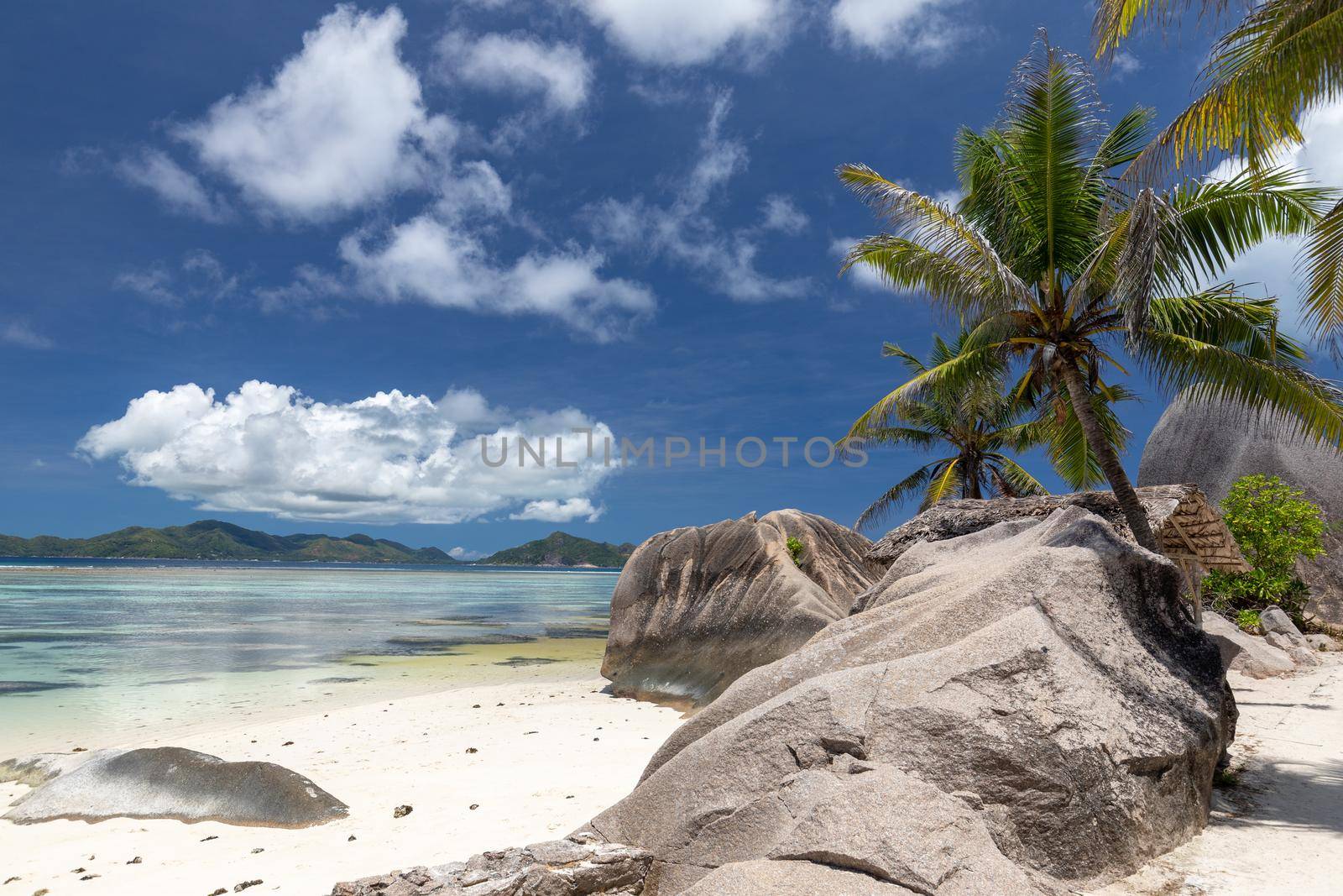 Beautiful beach Anse Source D'Argent on Seychelles island La Digue with white sand, granite rocks on the beach, palm trees, wooden cottage and blue sky with white clouds