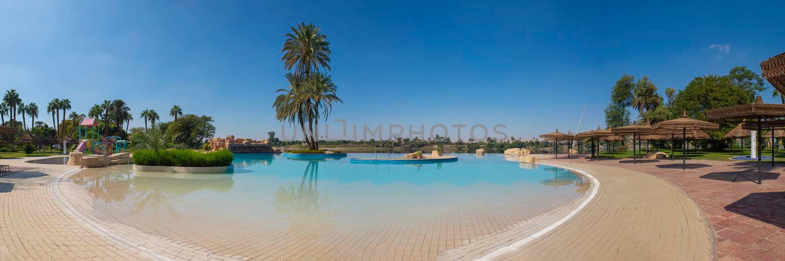 Panoramic view with tall large date palm tree phoenix dactylifera on island in infinity swimming pool at luxury tropical hotel resort
