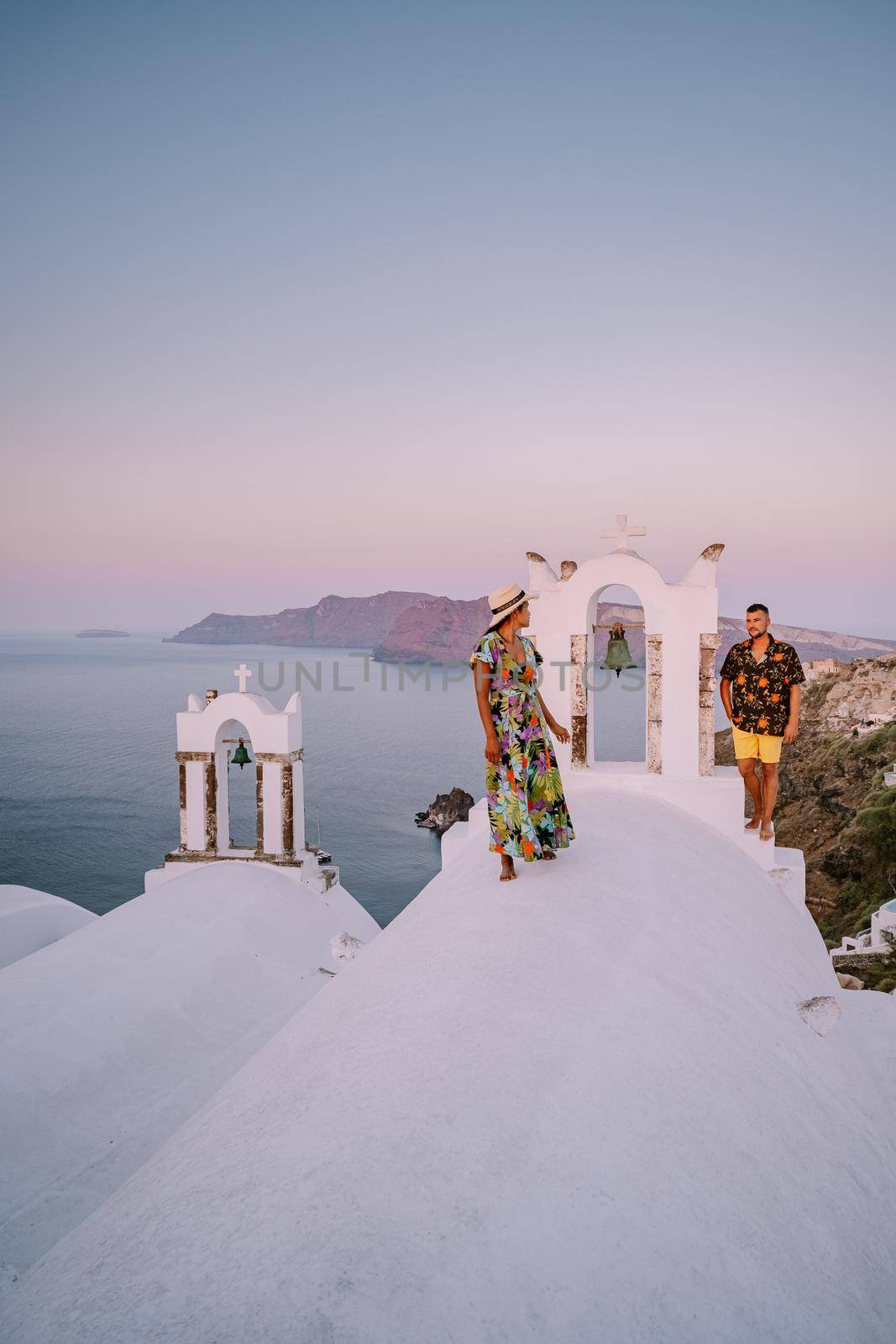 Santorini Greece, young couple on luxury vacation at the Island of Santorini watching sunrise by the blue dome church and whitewashed village of Oia Santorini Greece . Europe