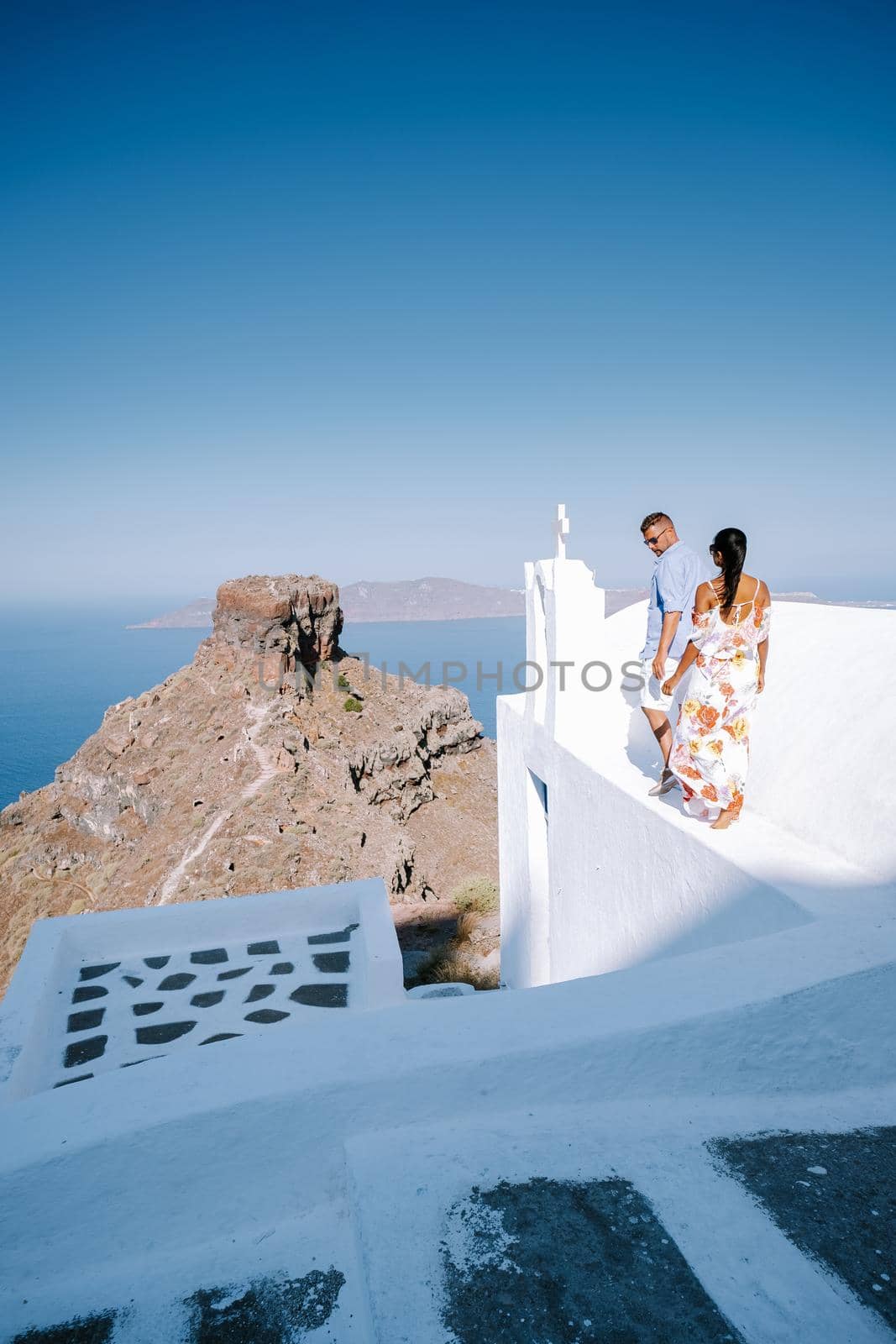 couple visit Skaros rock Fira, Santorini Greece, young couple on luxury vacation at the Island of Santorini watching sunrise by the blue dome church and whitewashed village of Oia Santorini Greece  by fokkebok