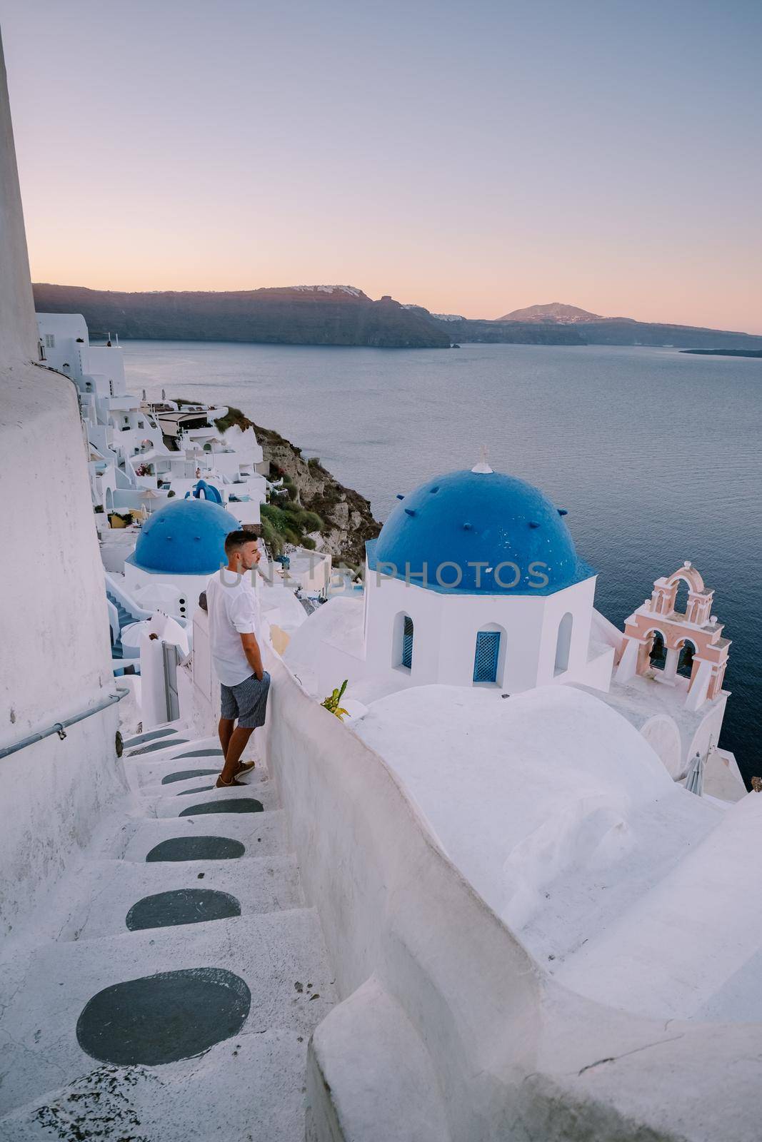 Sunset at the Island Of Santorini Greece, beautiful whitewashed village Oia with church and windmill during sunset, young men on luxury vacation Santorini by fokkebok